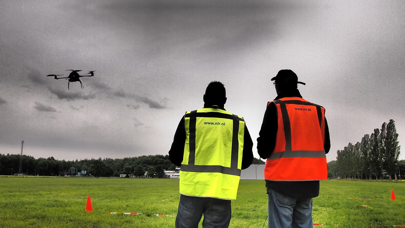 Two pilots in hi-vis vests flying a training drone over an airfield